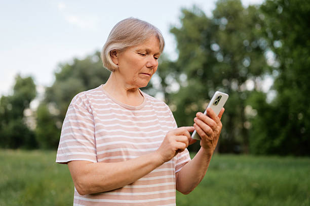 istock A thoughtful middle-aged woman with light, short hair is seen outdoors, looking down and interacting with a smartphone, with a blurred green natural background. 2228744636
