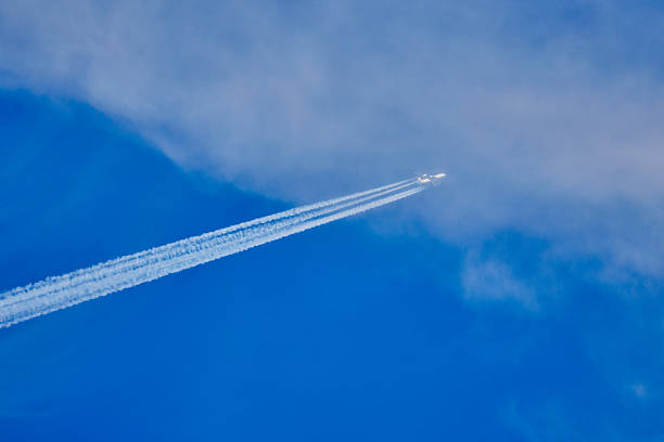 a plane climbing with tracks behind it in the blue sky