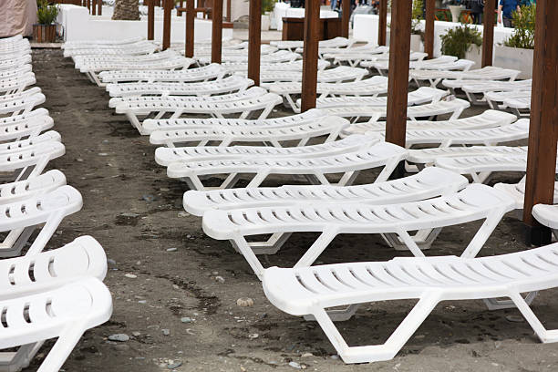 A row of white lounge chairs are lined up on a beach. The chairs are empty and the beach is empty