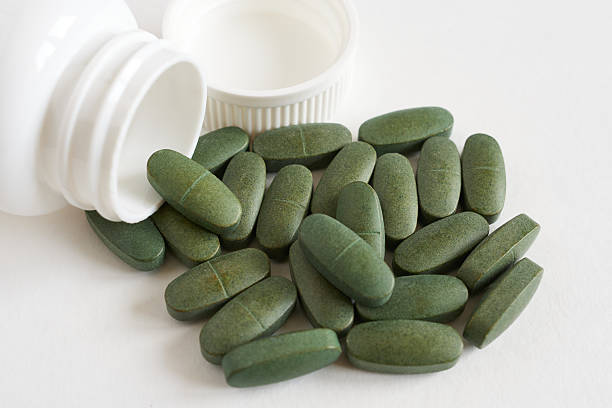istock Green pills spilling out of a white plastic container on a white background 2228751140