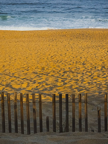 istock Wooden fence casting shadows on sandy beach at sunset light 2228751181