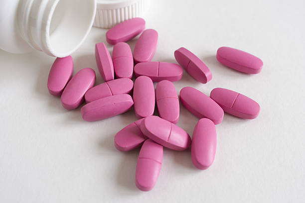 istock pink pills and bottle on white background. Focus on foreground, soft bokeh. 2228751240