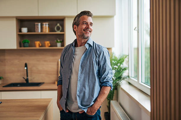 istock Happy mature man smiling and looking away while standing in kitchen 2228754426