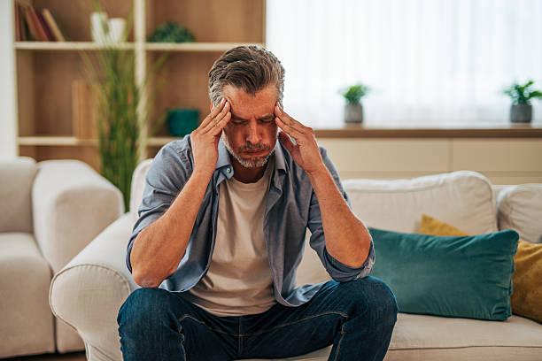 istock Mature man suffering from headache while sitting on sofa at home 2228754469