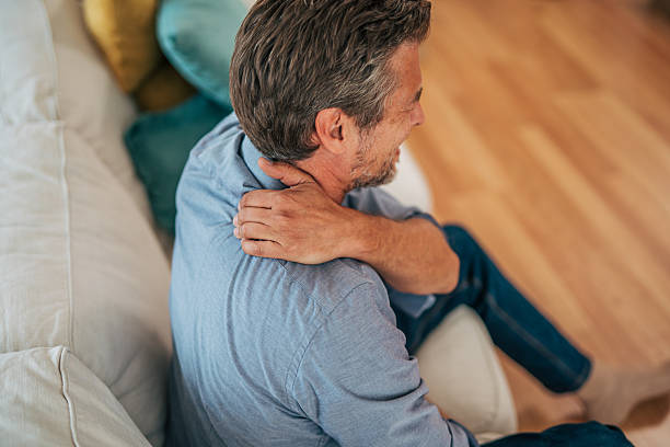 istock Mature man suffering from neck pain while sitting on sofa 2228754815