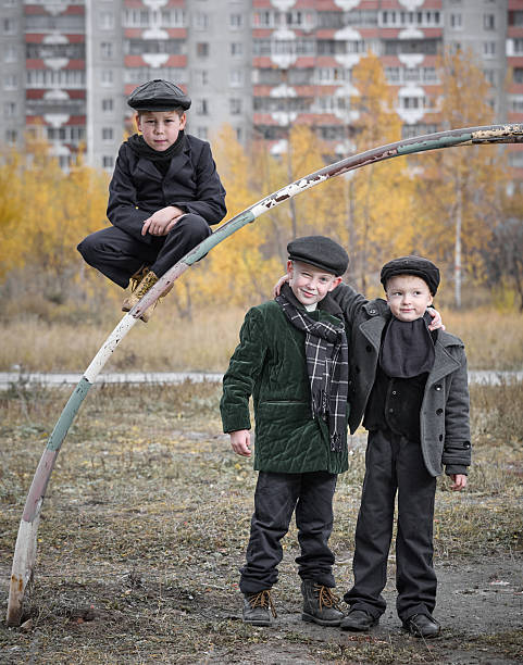 Three cheerful elementary age kids dressed in retro-style clothing spending time and having fun together at a old playground in the residential district in overcast autumn day