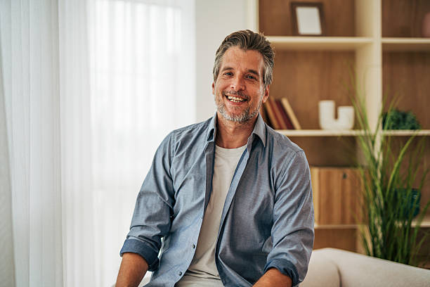 istock Smiling mature man sitting on sofa at home looking at camera 2228756954