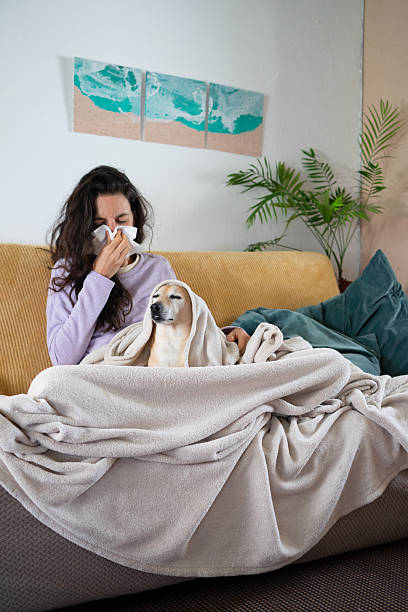 Sick woman blowing nose while sitting on sofa with dog
