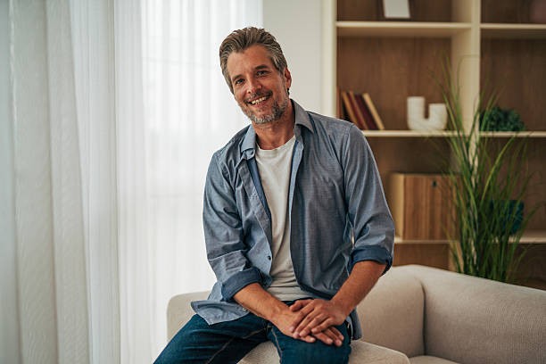 istock Smiling mature man sitting on sofa at home looking at camera 2228757196