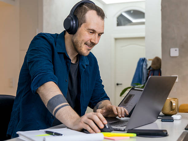 istock Young man engaged in remote work while using a laptop and headphones in a modern home office setup 2228759352