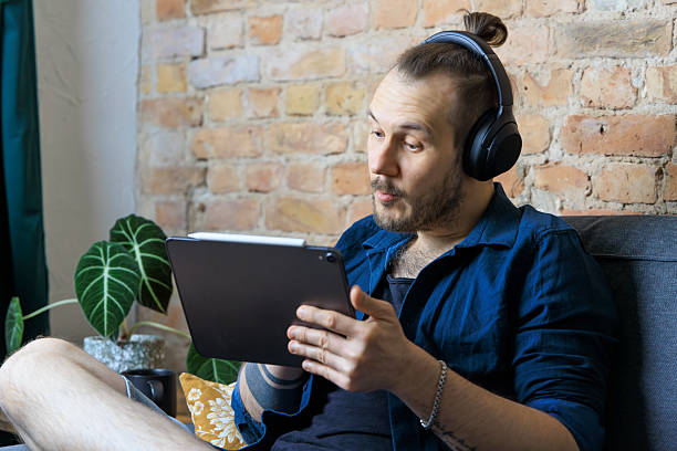 istock Man with headphones holds tablet, chatting in front of brick wall 2228761792