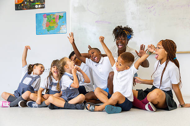 Happy multi-ethnic students and teacher are sitting on the floor of a classroom, laughing and raising their arms