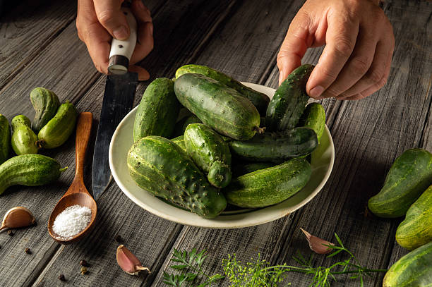 istock Fresh cucumbers are arranged in a bowl while hands grasp additional cucumbers. Surrounding ingredients like garlic and salt create a natural cooking atmosphere 2228763513