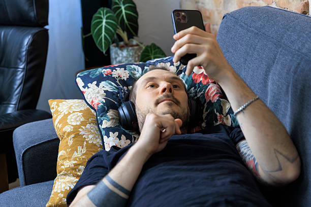 istock Man is lying on couch in living room using a smartphone 2228763632