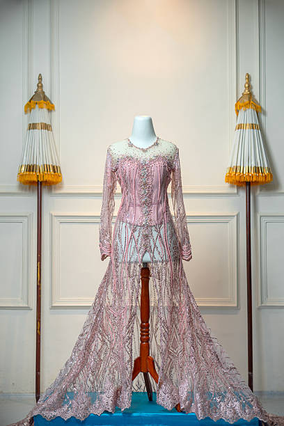 istock A luxurious pink wedding gown with intricate sequin and bead embellishments, displayed on a mannequin with traditional ceremonial umbrellas in a clean and elegant setting. 2228764549