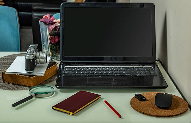 Laptop computer with notebook, magnifier, pencil, usb drive and old camera on the office desk.
