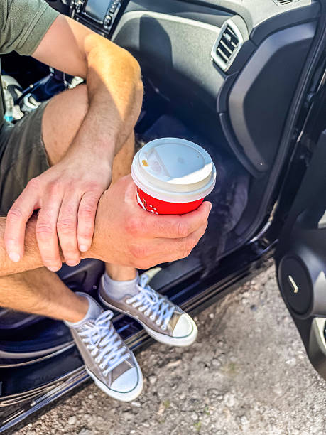 Man relaxing with takeaway coffee cup sitting in car doorway