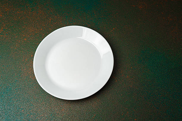 istock Empty white plate on textured green background with natural lighting display 2228770385