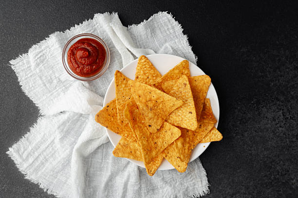 Nacho chips on plate with tomato sauce on white cloth and black background