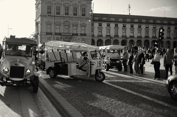 Lisbon, Portugal - November 2, 2024: A tuk-tuk driver parks his tuk-tuk at the Praça do Comércio square in Lisbon downtown.