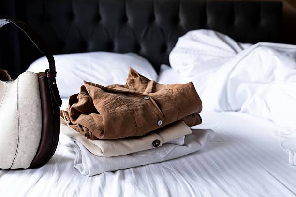 istock Neatly folded clothes and bag on white bedding in cozy bedroom 2228771366