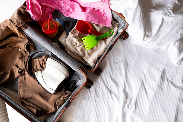istock Open suitcase with summer clothes and beach toys on bed 2228772033