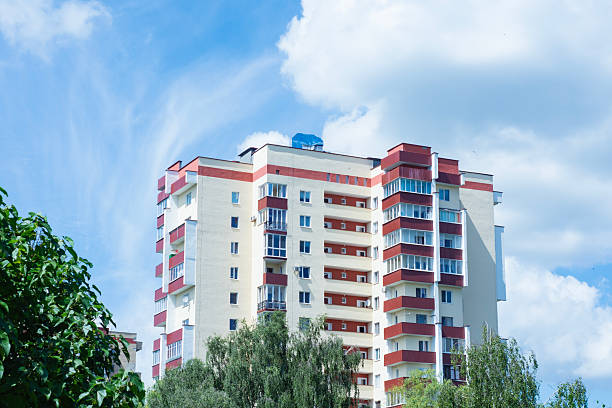 istock A multi-story residential apartment building with red balconies and a light facade rises above lush green trees under a bright blue sky. 2228773043