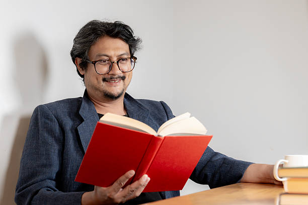 istock Young man with glasses reading book at home 2228773122