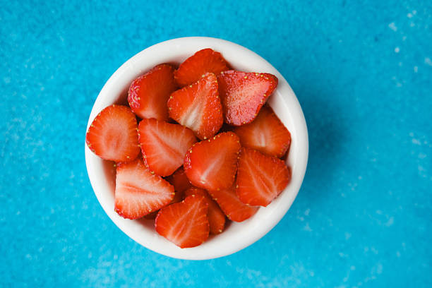 bowl of fresh sliced strawberries on blue textured background