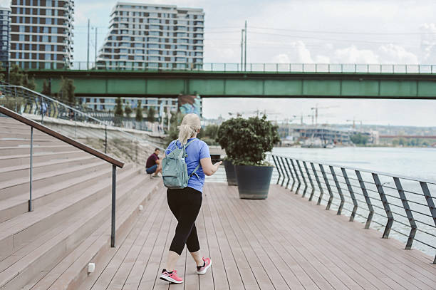 istock Senior Woman Jogging by Riverside Bridge with Smartphone Holder 2228780973