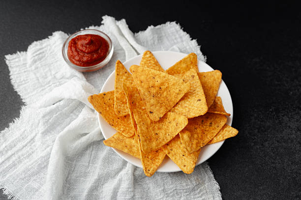 istock Nacho chips on plate with tomato sauce on white cloth and black background 2228781283