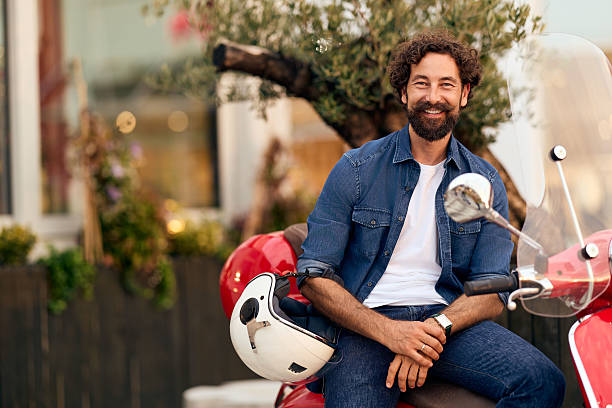 Happy bearded man enjoying leisure time outdoors, sitting on a red scooter passionately.