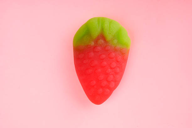 Gummy candy shaped like a strawberry with green leaves on a pink background represents sweetness and indulgence
