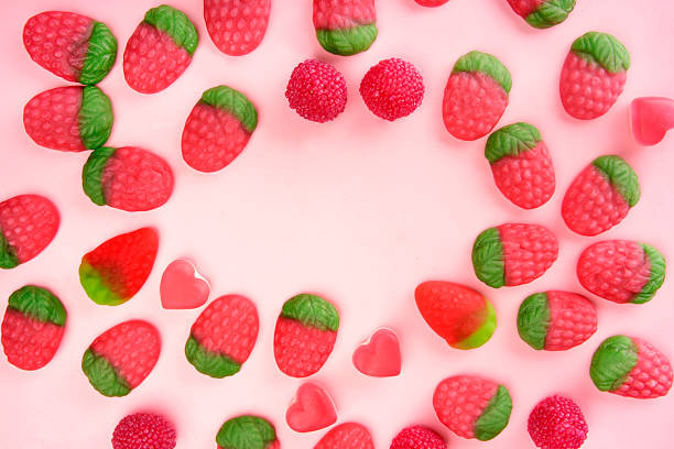 Frame of gummy candy strawberries and hearts creating copy space on pink background