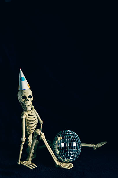 A humorous image of a Halloween skeleton in a party hat with a disco ball sitting with lots of room for copy on a black background.