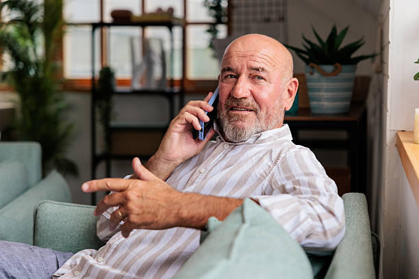 istock Smiling Man Sitting on Sofa Talking on Phone 2228787939