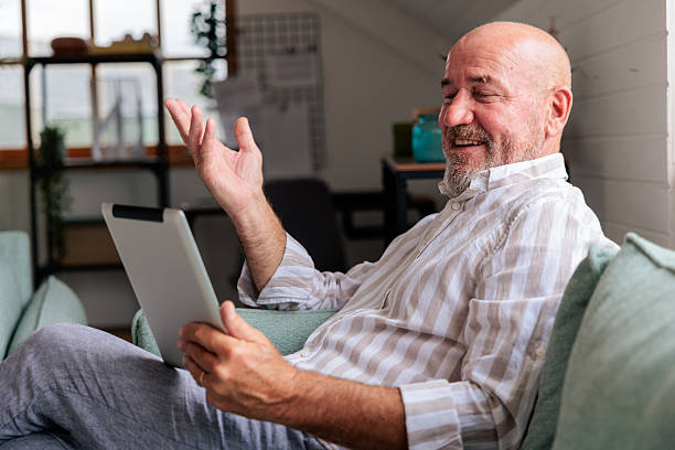 istock Man Sitting on Sofa with Tablet and Earbuds on Video Call 2228790157