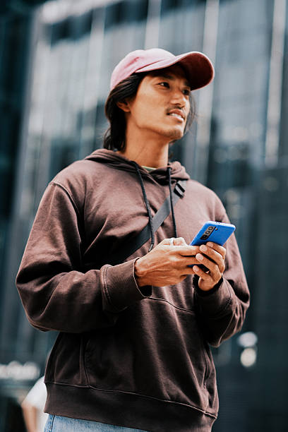 istock Smiling Young Asian Man Using Smartphone Outdoors in Urban Cityscape 2228793870
