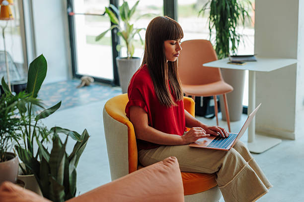 istock Young woman working on laptop in modern office lobby 2228796200