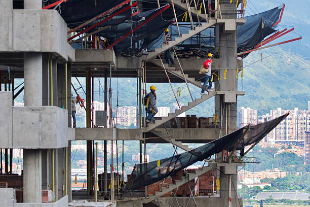 Workers at the very top of a building under construction with a hill in the background on which there are other buildings in Medellin.