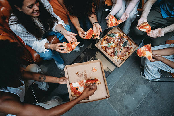 Group of friends sharing delicious pizza slices, laughing and enjoying each other's company during a lively social gathering