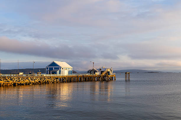 Tranquil water reflects a pier and a blue waterfront building at sunset.