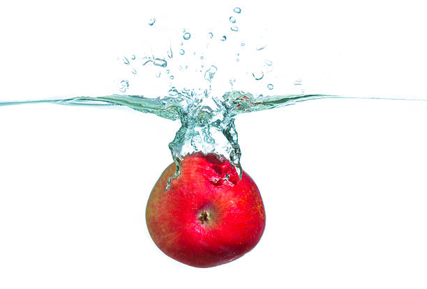 Close-up view of a vibrant red apple splashing into crystal-clear water, creating dynamic bubbles and ripples in a bright white background.