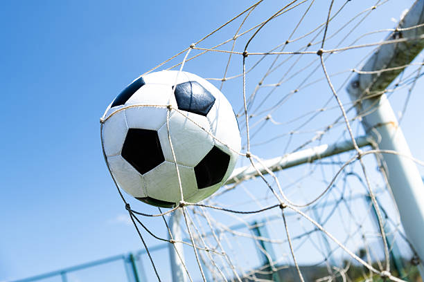 istock Soccer ball hitting the goal net against blue sky background 2228805425