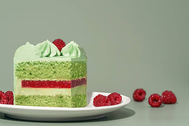 istock Layered bento cake featuring vibrant raspberry and pistachio sponge, adorned with delicate mint frosting and fresh raspberries, presented on a white plate against a soft green backdrop 2228813884