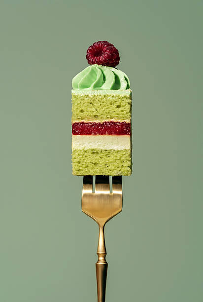 istock Layered bento cake featuring vibrant raspberry and pistachio sponge, topped with creamy frosting and a fresh raspberry, elegantly presented on a golden fork against a soft green background 2228813902