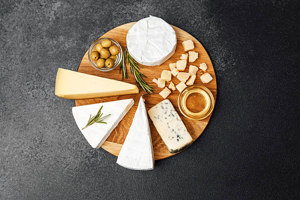 A selection of cheeses, olives, and honey is beautifully arranged on a wooden board.
