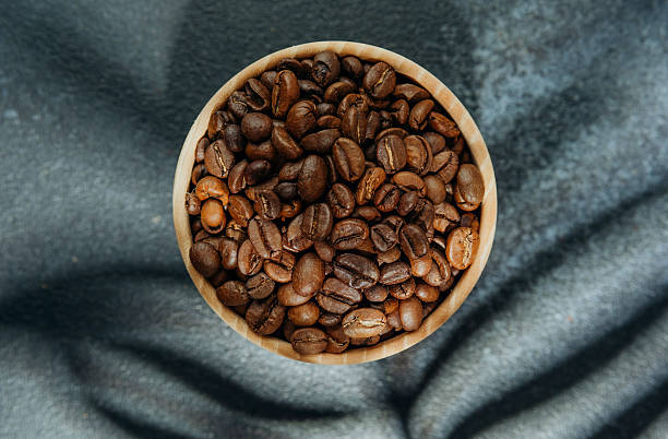 istock Coffee beans in wooden bowl with leaf shadow on dark background 2228816484