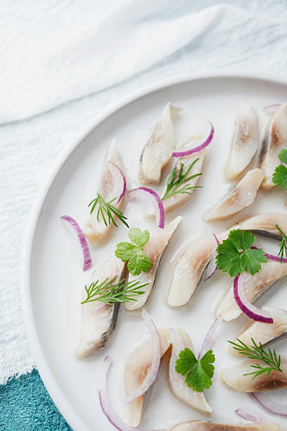 istock Marinated herring slices with red onion and herbs on white plate with napkin over blue background 2228816517
