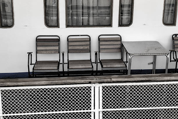 Deck chairs and a table remain unoccupied on a ferry, positioned against a backdrop of a calm sea and gentle waves, creating a serene atmosphere for travelers.